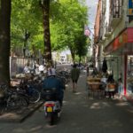 Amsterdam Bikes - a person riding a scooter down a sidewalk