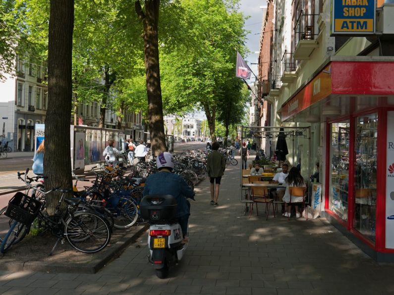 Amsterdam Bikes - a person riding a scooter down a sidewalk