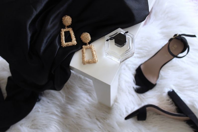 Secluded Luxury - pair of gold-colored earrings on table and black ankle-strap pumps on area rug