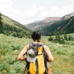 Travel Backpack - person carrying yellow and black backpack walking between green plants