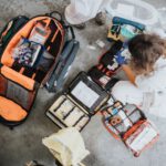 Emergency Kit - boy in white shirt sitting on orange and black backpack