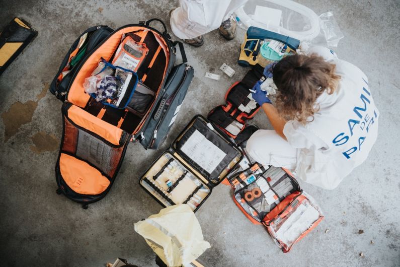 Emergency Kit - boy in white shirt sitting on orange and black backpack