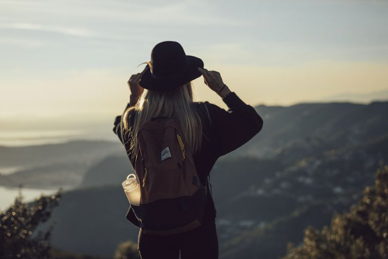 Solo Travel - woman in gray hoodie and black pants wearing black hat standing on top of mountain during