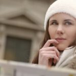 Family Road Trip - Concentrated female in warm hat and coat looking for right way while standing with map in street