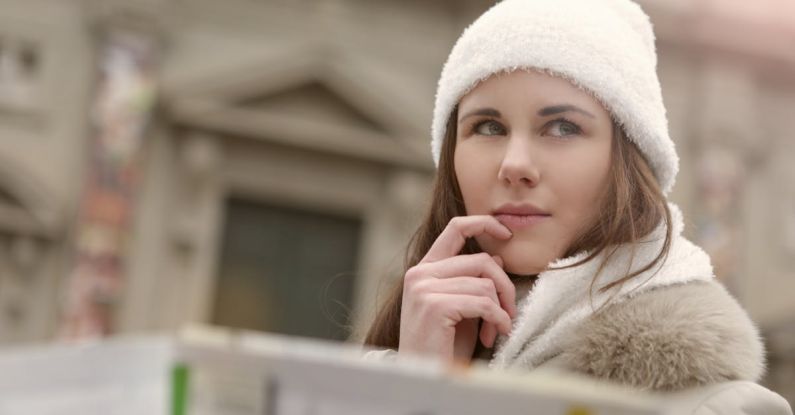 Family Road Trip - Concentrated female in warm hat and coat looking for right way while standing with map in street