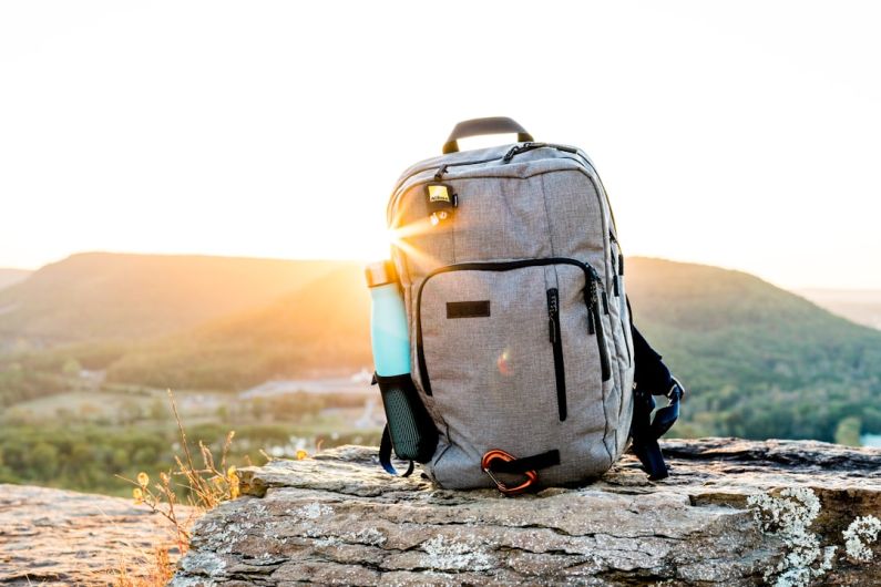 Backpack - grey and black hiking backpack and cyan tumbler on grey rock during sunset