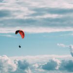 Parachute - person in red parachute under white clouds during daytime