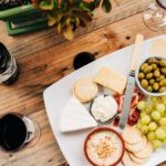 Cheese Board - fruits and meats on white ceramic plate beside wine glass and bottle