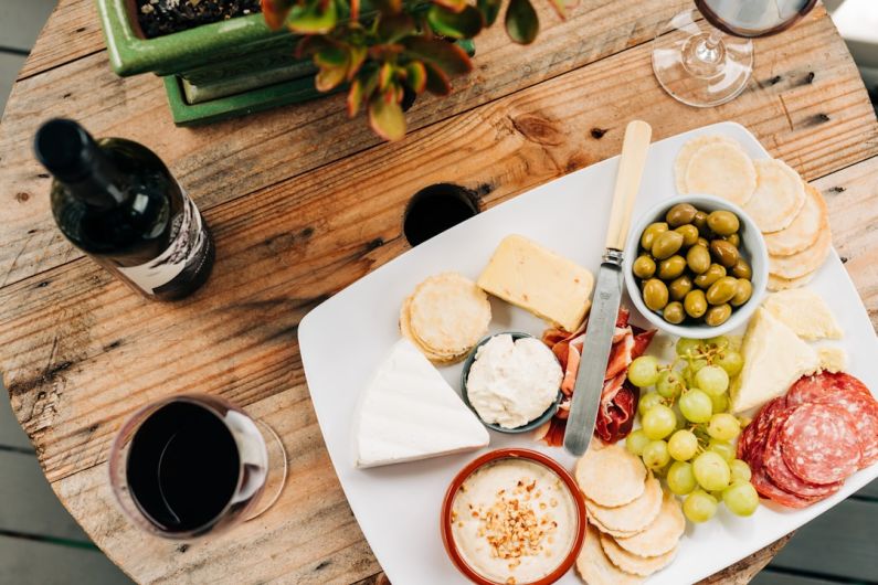 Cheese Board - fruits and meats on white ceramic plate beside wine glass and bottle