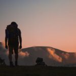 Backpack Journey - silhouette of man walking along field leading to mountain